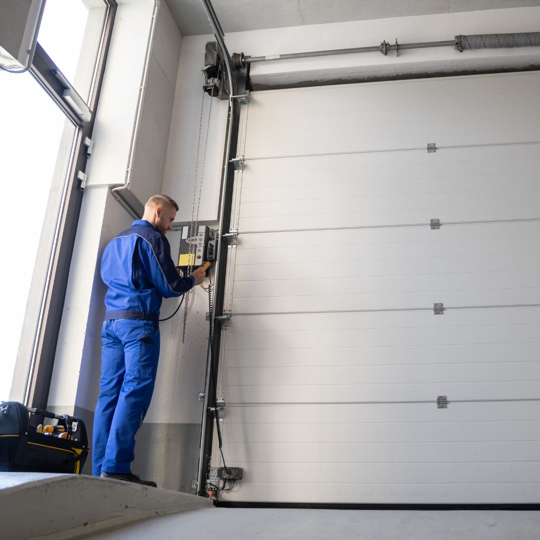 Technician working on a white garage door near the wall controls