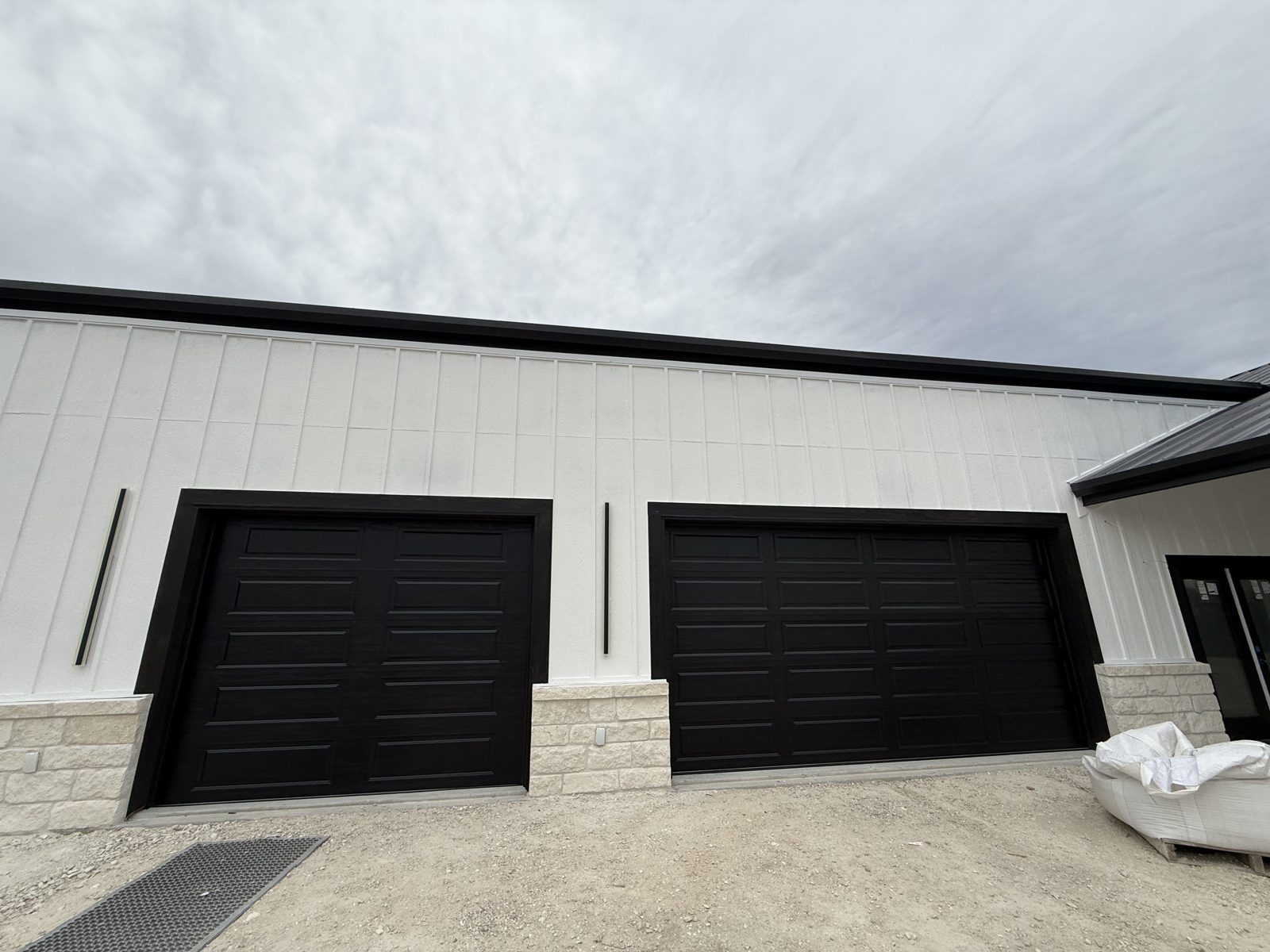 New black C.H.I. 18x8 and 10x8 long-panel garage doors on a new construction home with white board-and-batten siding in Seguin, TX