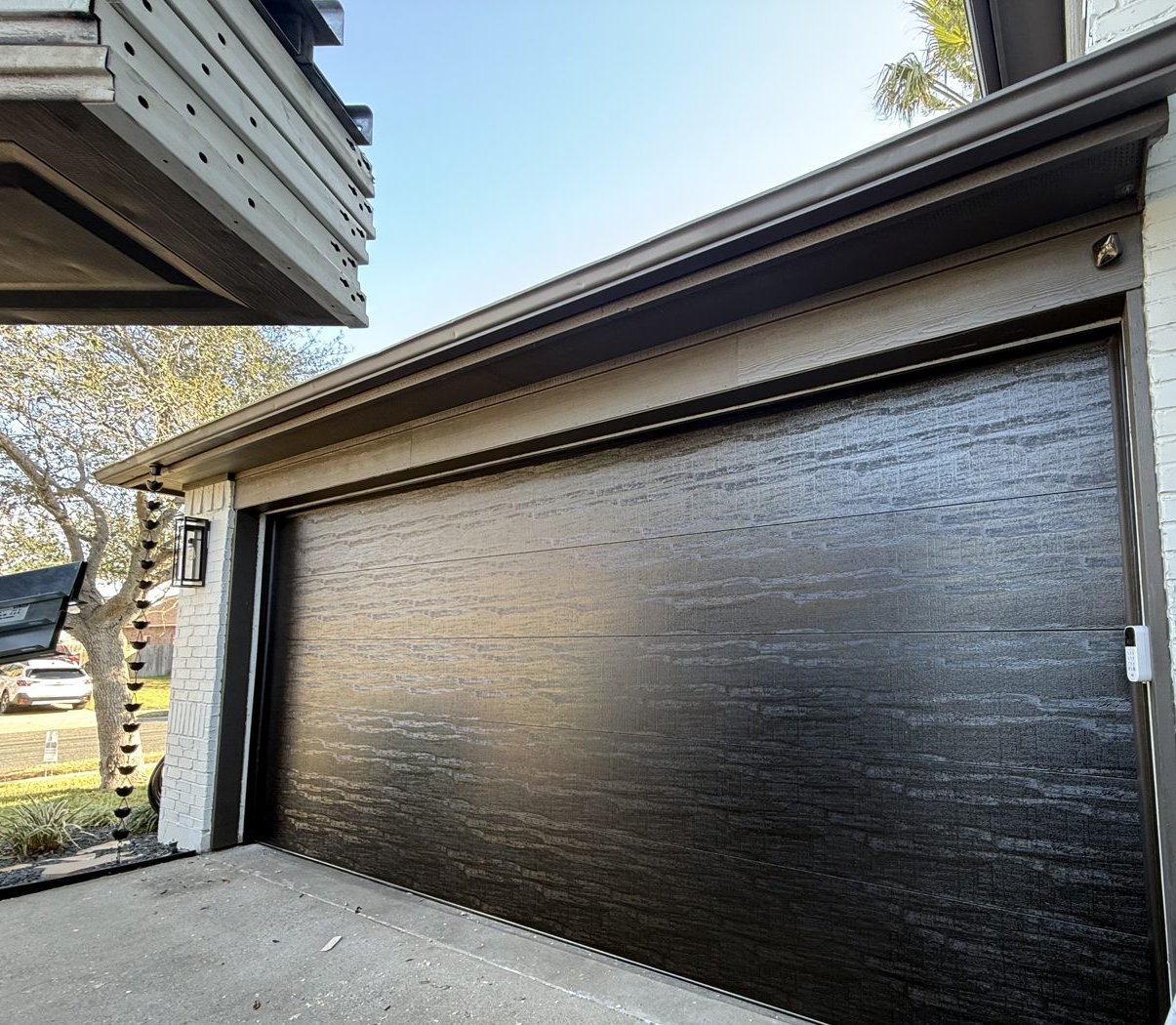 New C.H.I. 18x8 black flush panel insulated garage door on a white brick home in Buda, TX