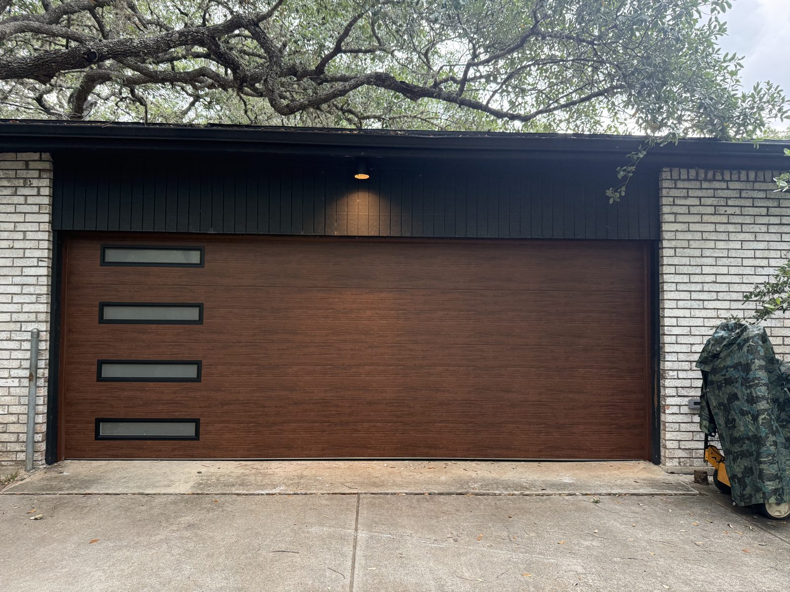 New Clopay 16x7 walnut finish steel-back insulated garage door with windows on a white brick home in San Marcos, TX