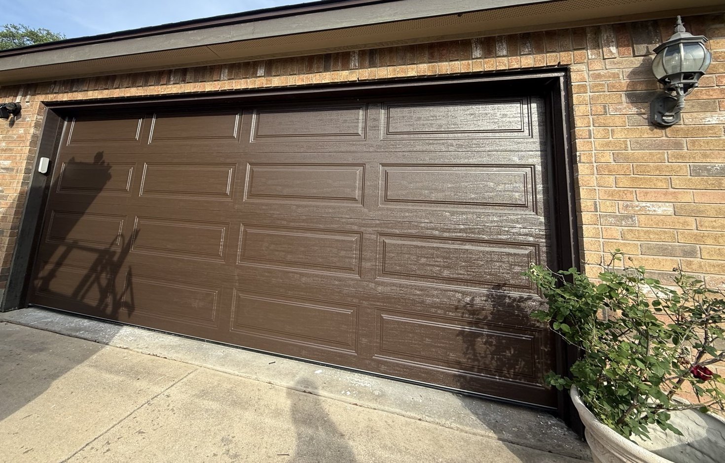 New 16x7 brown steel-back insulated raised panel garage door on a brick home in Kyle, TX